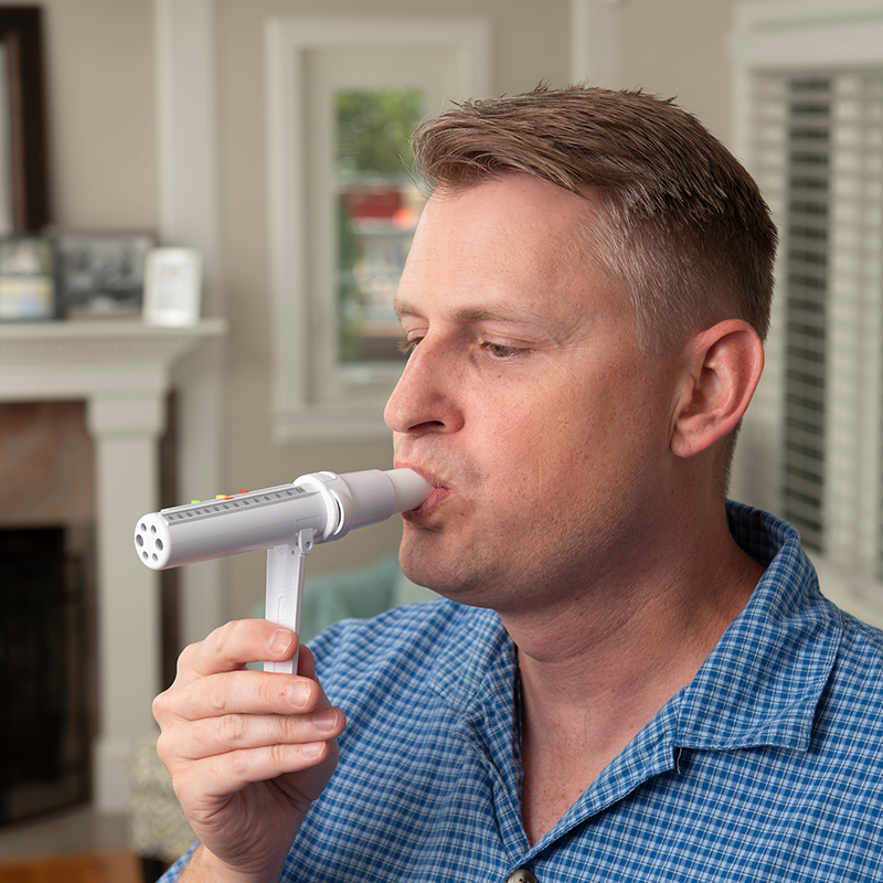 Man in checkered blue shirt blowing into White PeakAir Peak Flow Meter unit
