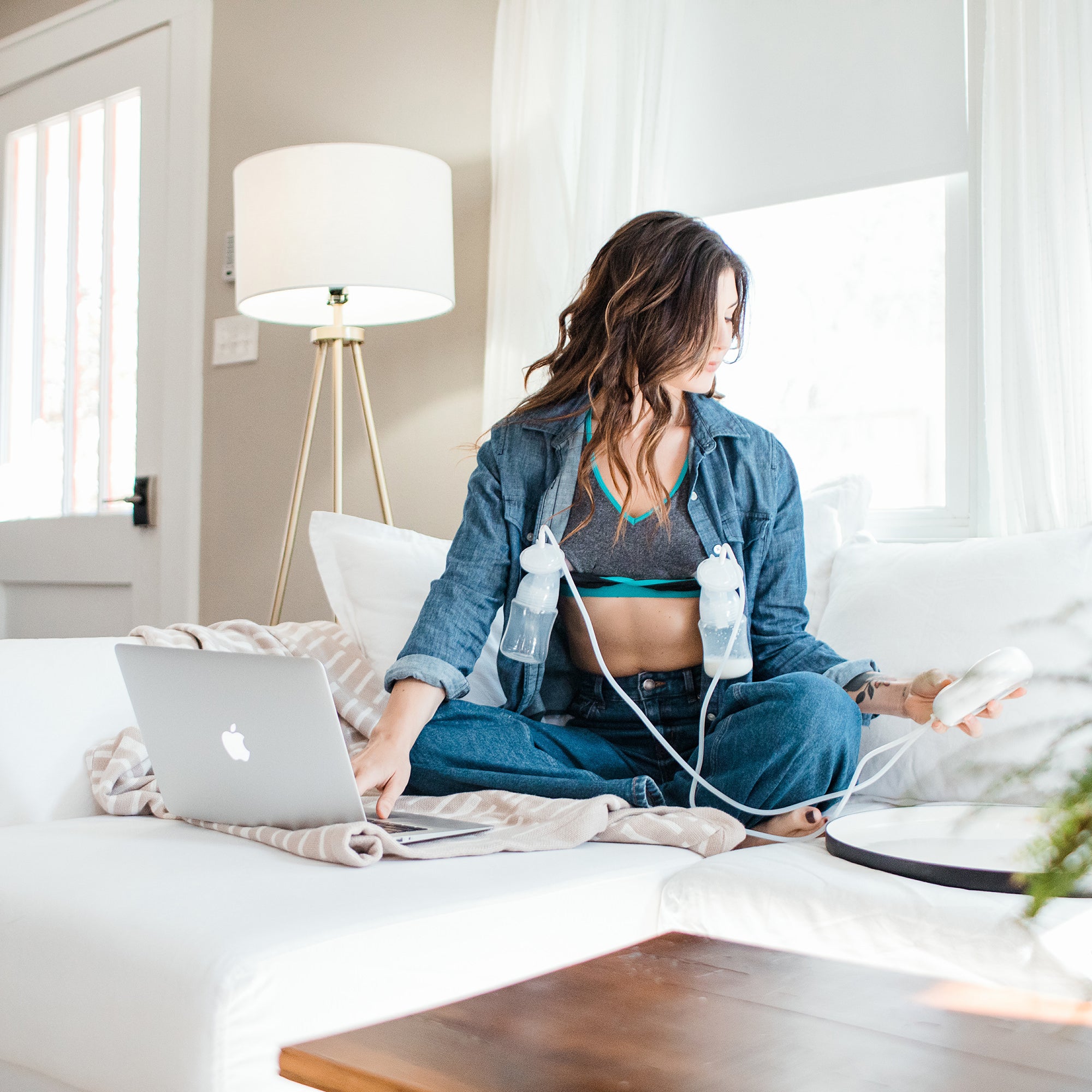 Woman Sitting On Couch Using Laptop And Using Motif Medical Duo Double Electric Breast Pump And Hands Free Bra