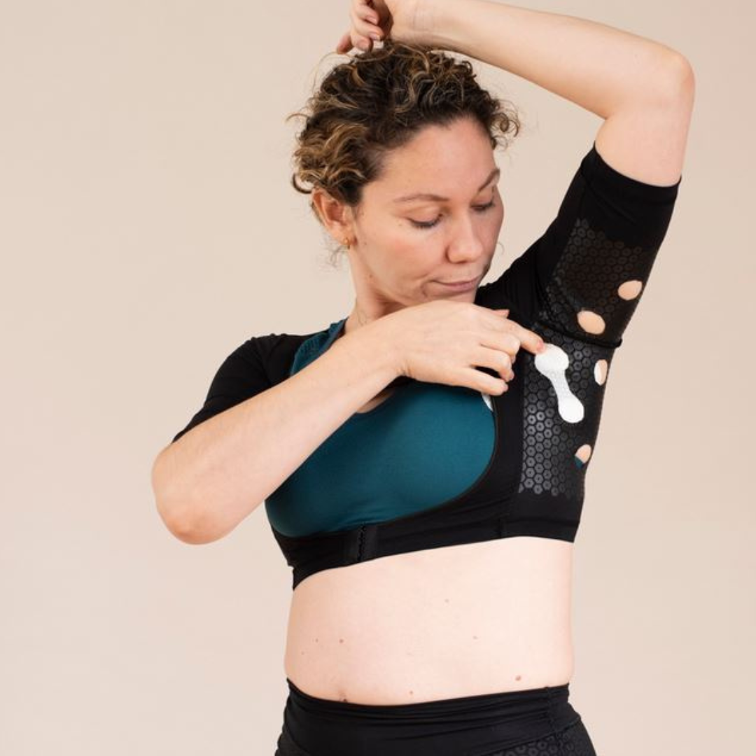 Woman wearing HidraWear AX Crop Top with arm raised and inserting the HidraWear Dressing in place under the arm