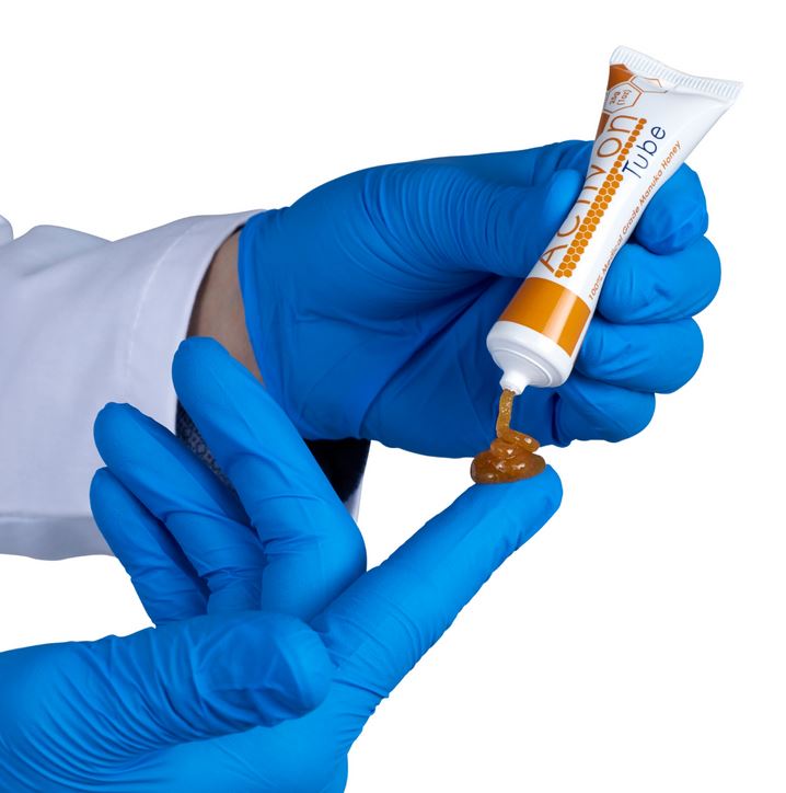 A person wearing gloves squeezing product from the Activon Honey Tube