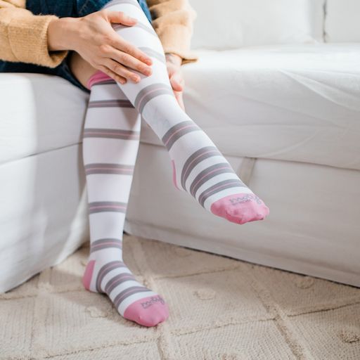 Close up of woman wearing tall white socks with grey and pink stripes with pink top band,heel and toe caps-Motif Medical Gradient Maternity Compression Socks