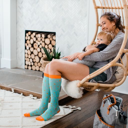 Woman holding child and wearing mint green tall socks with orange and pink triangles and orange top band, toe and heel caps - Motif Medical Gradient Maternity Compression Socks