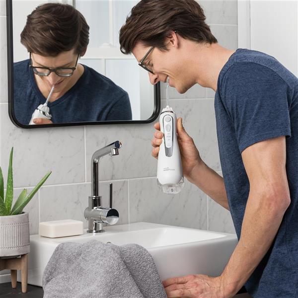 Man standing at a bathroom sink using Waterpik Cordless Advanced Water Flosser in Pearly White